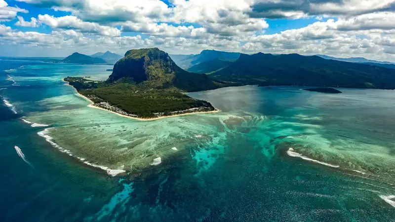 Türkisfarbene Lagune vor Le Morne auf Mauritius mit grünem Bergmassiv, Riffkante und palmengesäumtem Strand