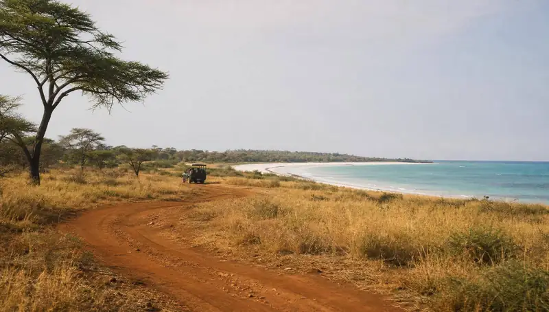 Safari-Fahrzeug am weiten Strand mit türkisfarbenem Meer in Afrika